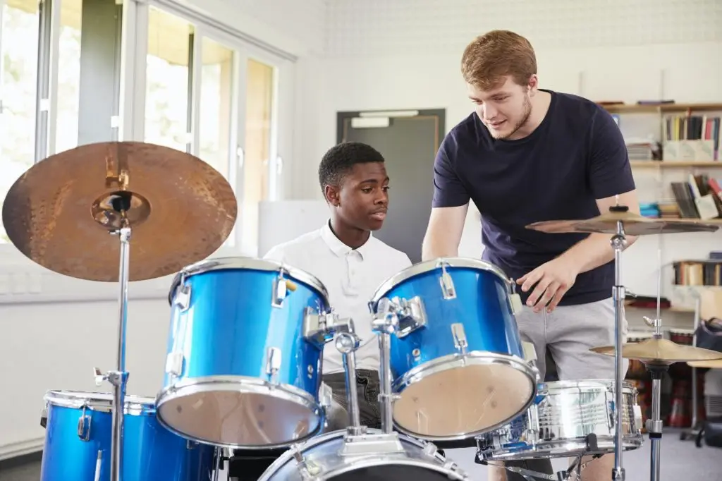 Male Pupil With Teacher Playing Drums In Music Lesson